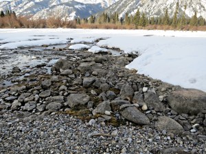 A stony beach kept clear of snow by the warm spring emerging into the river