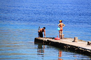 Local guy tenderises the squid he has just caught while his missus waits with plastic bag to take it home
