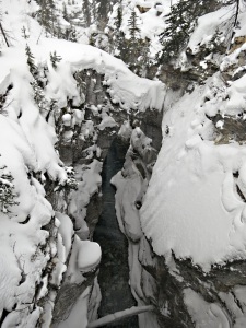 A natural rock bridge high above the water, topped by a thick layer of snow