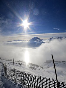 At the top of the ridge above the cloud bands, tiny ice crystals visible against the blue, a shaft of light like a laser beam lit by the sun shafting down through the cloud which is made up of the ice crystals. 
