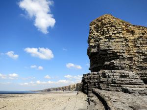 Rounding the promontory, cliffs curving westwards to the next headland, wide expanse of rock and sand exposed at low water.