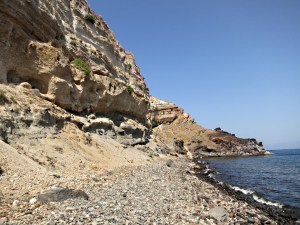 The eroded pumice starts to form a loose scree, straight ahead the lava extrusion juts out into the sea